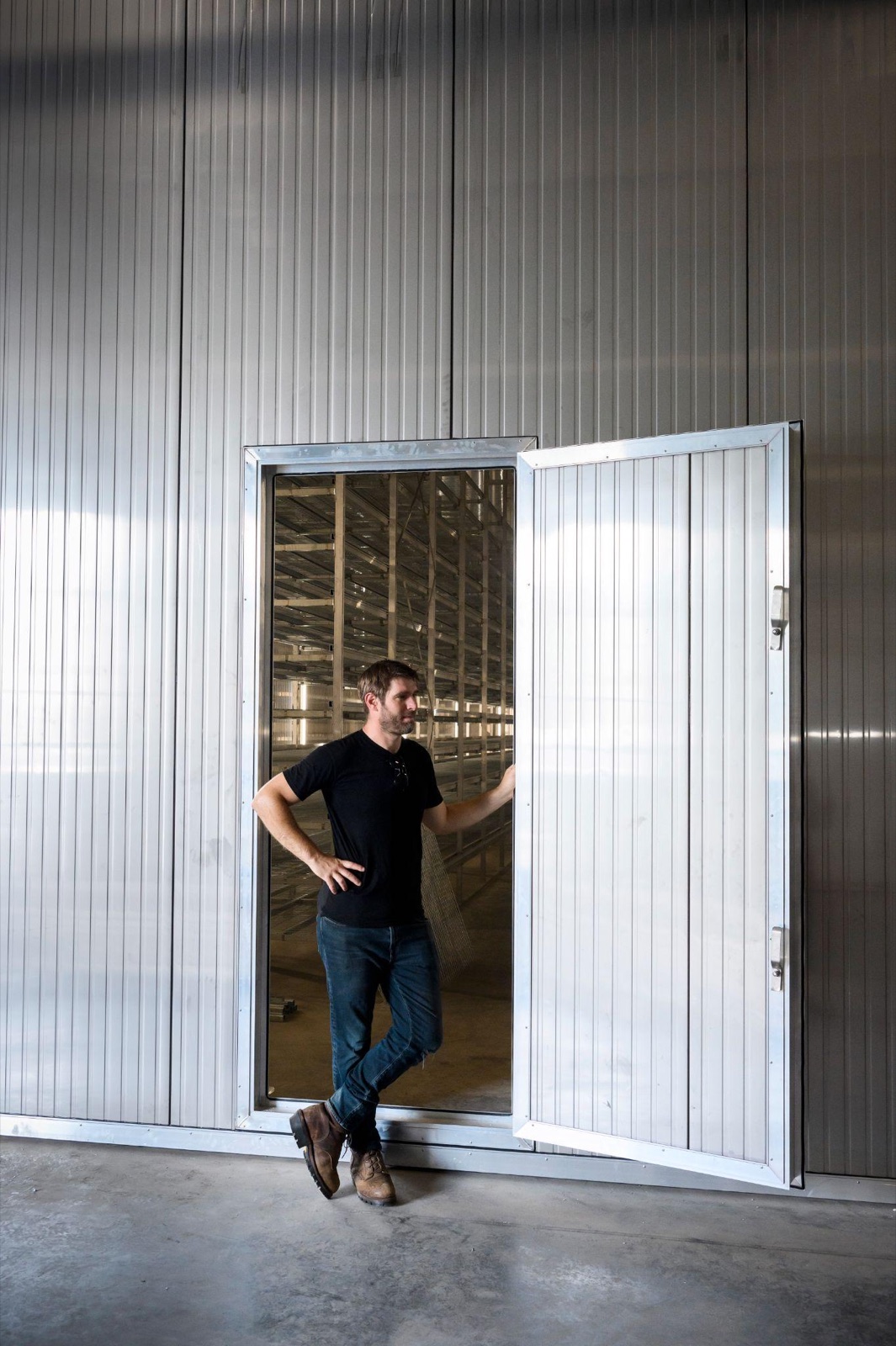 A person standing at the open door of the AirMycelium grow room, with vertical growing racks visible inside